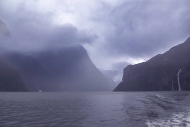 Yeni Zelanda 'nın Güney Adası' ndaki Fiordland Ulusal Parkı 'ndaki Milford Sound' da bulutların ve sisin içindeki dağların fotoğrafı.