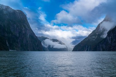 Yeni Zelanda 'nın Güney Adası' ndaki Fiordland Ulusal Parkı 'ndaki Milford Sound' da bulutların ve sisin içindeki dağların fotoğrafı.