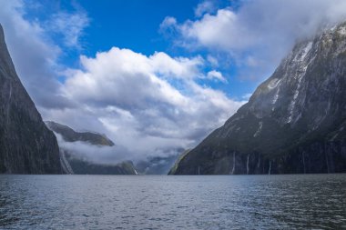 Yeni Zelanda 'nın Güney Adası' ndaki Fiordland Ulusal Parkı 'ndaki Milford Sound' da bulutların ve sisin içindeki dağların fotoğrafı.