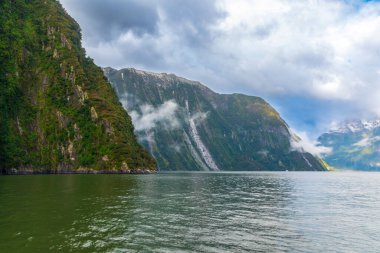 Yeni Zelanda 'nın Güney Adası' ndaki Fiordland Ulusal Parkı 'ndaki Milford Sound' da bulutların ve sisin içindeki dağların fotoğrafı.