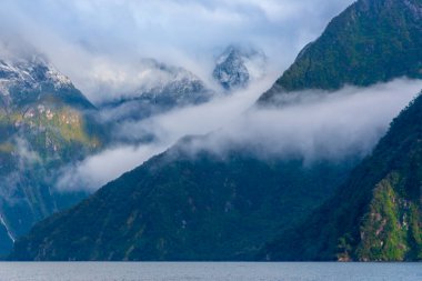 Yeni Zelanda 'nın Güney Adası' ndaki Fiordland Ulusal Parkı 'ndaki Milford Sound' da bulutların ve sisin içindeki dağların fotoğrafı.