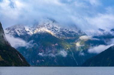 Yeni Zelanda 'nın Güney Adası' ndaki Fiordland Ulusal Parkı 'ndaki Milford Sound' da bulutların ve sisin içindeki dağların fotoğrafı.