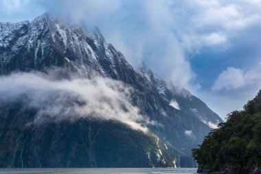 Yeni Zelanda 'nın Güney Adası' ndaki Fiordland Ulusal Parkı 'ndaki Milford Sound' da bulutların ve sisin içindeki dağların fotoğrafı.