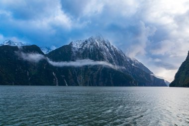 Yeni Zelanda 'nın Güney Adası' ndaki Fiordland Ulusal Parkı 'ndaki Milford Sound' da bulutların ve sisin içindeki dağların fotoğrafı.