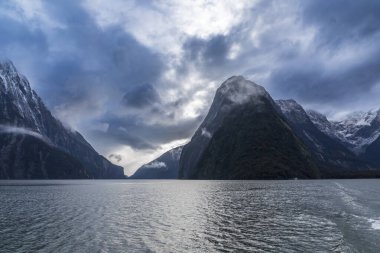 Yeni Zelanda 'nın Güney Adası' ndaki Fiordland Ulusal Parkı 'ndaki Milford Sound' da bulutların ve sisin içindeki dağların fotoğrafı.