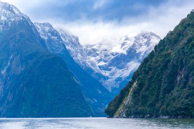 Yeni Zelanda 'nın Güney Adası' ndaki Fiordland Ulusal Parkı 'ndaki Milford Sound' da bulutların ve sisin içindeki dağların fotoğrafı.