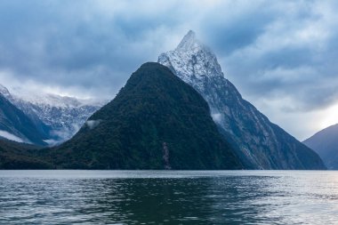 Yeni Zelanda 'nın Güney Adası' ndaki Fiordland Ulusal Parkı 'ndaki Milford Sound' da bulutların ve sisin içindeki dağların fotoğrafı.
