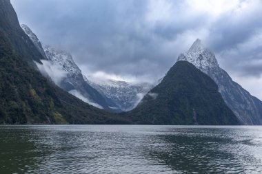 Yeni Zelanda 'nın Güney Adası' ndaki Fiordland Ulusal Parkı 'ndaki Milford Sound' da bulutların ve sisin içindeki dağların fotoğrafı.
