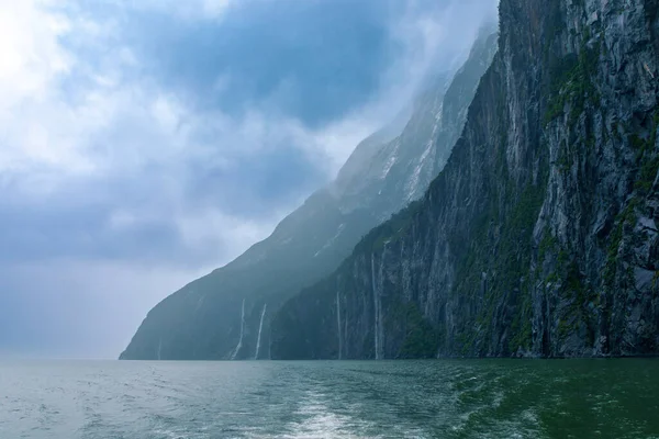 Yeni Zelanda 'nın Güney Adası' ndaki Fiordland Ulusal Parkı 'ndaki Milford Sound' da bulutların ve sisin içindeki dağların fotoğrafı.