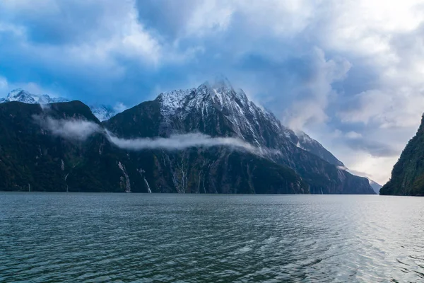 Yeni Zelanda 'nın Güney Adası' ndaki Fiordland Ulusal Parkı 'ndaki Milford Sound' da bulutların ve sisin içindeki dağların fotoğrafı.