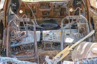 Büyük bir ormandaki toprak bir yolda terk edilmiş, sonra da ateşe verilmiş ve yok edilmiş küçük bir arabanın fotoğrafı.