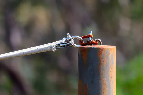 Photograph of a rusty shackle attached to a stainless steel connector on the top of a rusty painted steel post that is holding up a shade sail that is used for sun protection