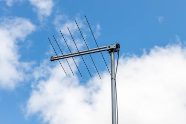 Konut evinin çatısındaki geleneksel bir televizyon anteninin fotoğrafı. Arka planda beyaz bulutlar olan mavi bir gökyüzüne karşı..