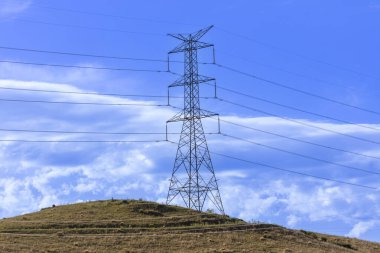 Avustralya 'nın parlak mavi gökyüzüne karşı çimenli bir tepedeki büyük bir elektrik iletim kulesinin fotoğrafı..