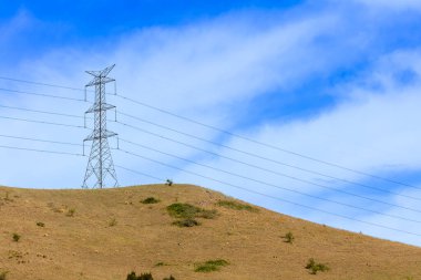 Avustralya 'nın parlak mavi gökyüzüne karşı çimenli bir tepedeki büyük bir elektrik iletim kulesinin fotoğrafı..