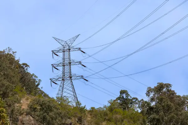 Avustralya 'nın parlak mavi gökyüzüne karşı çimenli bir tepedeki büyük bir elektrik iletim kulesinin fotoğrafı..