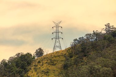 Avustralya 'nın turuncu gün batımında çimenli bir tepenin üzerindeki büyük bir elektrik iletim kulesinin fotoğrafı..