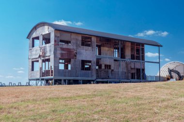 Avustralya 'da, parlak mavi bir gökyüzünün altında, yeşil bir çayırda harabeler içinde eski ve terk edilmiş çok katlı bir evin fotoğrafı..