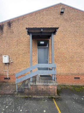 Eski ve bozulmuş ahşap bir merdiven girişinin fotoğrafı. Otoparktan büyük bir tuğla binanın yan duvarındaki kapıya bitişik..