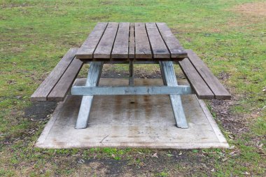 Aile büyüklüğünde ahşap ve çelik piknik masasının büyük bir halka açık kamp tesisinde yeterli oturma yeri olan sabit bir fotoğrafının çekilmesi..