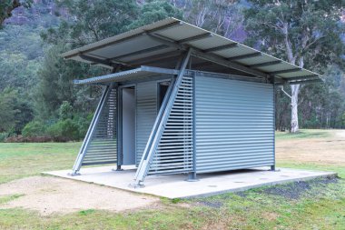 Halka açık bir kamp alanındaki beton bir üste oldukça iyi korunmuş çelik ve kıvrımlı demir uniseks tuvalet bloğunun fotoğrafı..