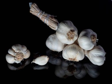 garlic in a bunch on a black background in the reflection in the base, a healthy plant for vegetarians and for cooking