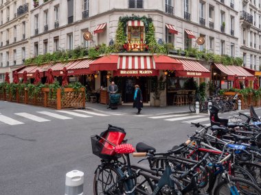 Paris, Fransa, 19 Nisan 2024: Turistler Paris Brasserie Martin restoranını ziyaret ediyor kırmızı renkli ve çiçek süslemeli, sokakta duran bisikletli, bavullu insanlar, EnrouteFrance
