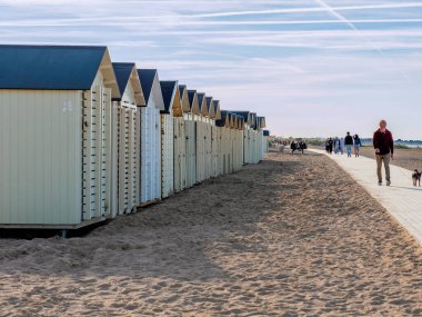 Ouistreham Normandy, kumsaldan manzara renkli ahşap evlerin yanında insanlar güneşli bir günde yürüyor, dinleniyor.