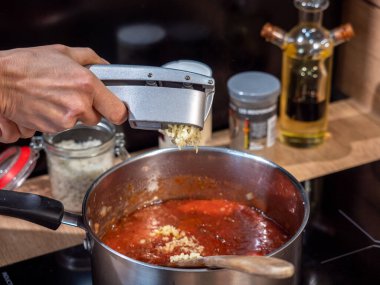 Özel bir metal sıkacağıyla sarımsak sıkmak, domates sosu pişirmek, arka planda metal kaplar.