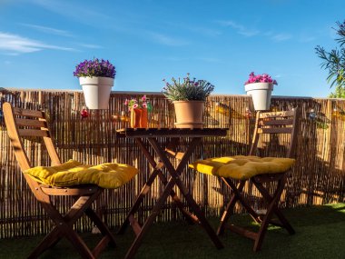 Günbatımında çiçeklerle dolu bir balkon, ahşap sandalyeli bir masa, dinlenmek için bir yer.