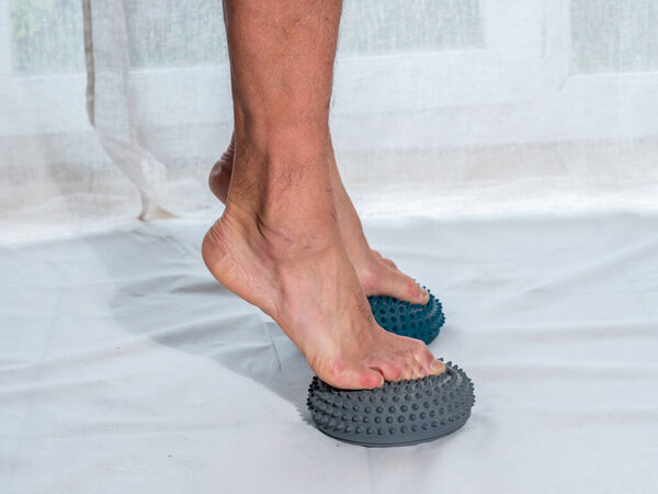 полушарие с шипами для реабилитации ног, улучшает кровообращение, стимулирует и массирует ноги, мужчина стоит впереди нажав на реабилитационное полушарие, легкий фон