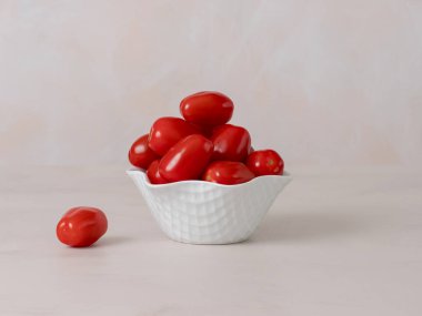 Beyaz kasede kırmızı kiraz domatesleri, A ve C vitaminleri antioksidanlardır, kasenin yanında bir vişneli domates, ön tarafta fotoğraf, açık arkaplan