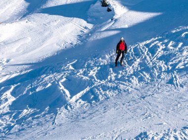 Chamonix, Fransa 20 Ocak 2025 Kırmızı ve siyah ceket giyen bir kayakçı veya dağcı, başlık ve gözlük karlı bir yamaçta duruyor. Bir elinde buz baltası tutuyor.