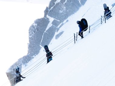 Chamonix-Mont-Blanc, Fransa, 21 Ocak 2025. Sırt çantalı ve paraşütlü insanlar Aiguille du Midi 'nin dik, karla kaplı yamacından paraşütle atlamak için inerler.