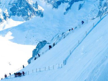 Chamonix-Mont-Blanc, Fransa, 21 Ocak 2025. Sırt çantalı ve paraşütlü insanlar Aiguille du Midi 'nin dik, karla kaplı yamacından paraşütle atlamak için inerler.