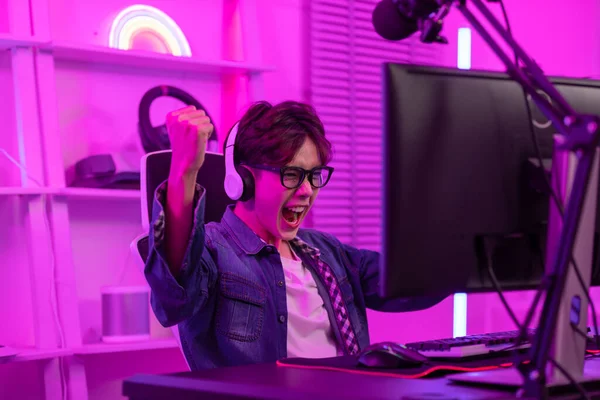 Asyalı oyuncu mutlu bir ifadeyle bilgisayar ekranı önünde yumruklarını kaldırdı ve online bir video oyunu kazanmasını kutladı. Profesyonel oyuncu konsepti
