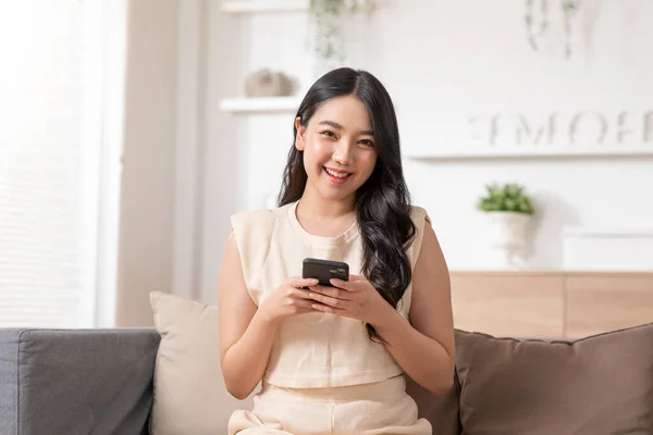 幸福起業家美しいビジネスアジアの若い女性は自宅でソーシャルメディアやラップトップでオンラインショッピングのためのカジュアルな使用の携帯電話を身に着けています — ストック写真