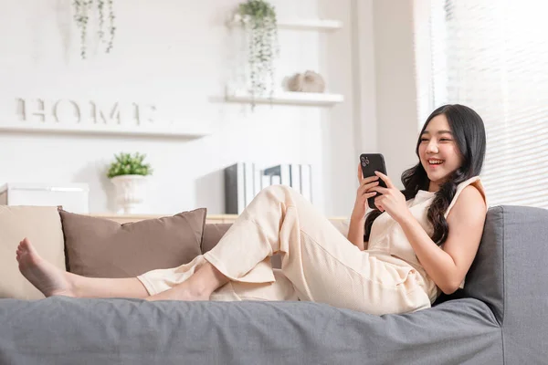 아시아인젊은 여성은 스마트폰 서핑을 이용해 웃으며 집에서 미디어나 온라인 쇼핑을 — 스톡 사진