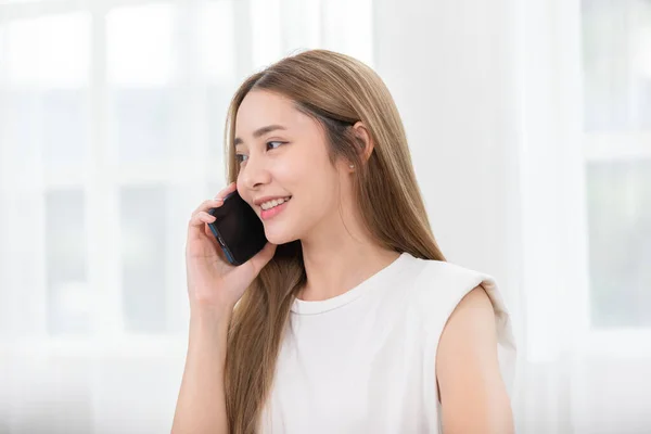 アジアの若い女性は 電話に答え 肯定的かつ幸福感と話をします スマートフォンの笑顔で魅力的な女性の話と家で良いニュースと良い瞬間で安心 — ストック写真