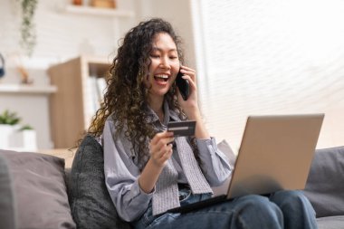 Genç bir kadın bilgisayardan online alışveriş yapmak için kredi kartı kullanıyor. İnternet mağazasından kıyafet almak için kredi kartı numarası yazıyor. Dijital ödeme teknolojisi kavramı.