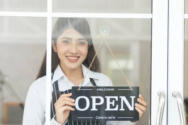 Female owner turning sign board to open coffee shop smile and happiness. Smiling asian woman open food and beverage cafe ready to service after quarantine due to virus pandemic. Small business
