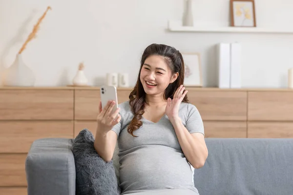 幸せな妊婦は居心地の良い家で家族と携帯電話でソファビデオ通話会議に座っています — ストック写真