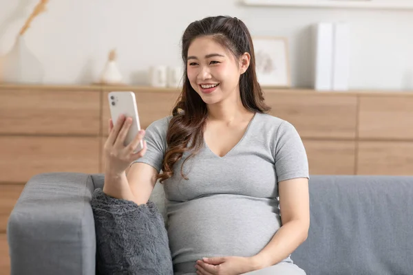 妊娠中のアジアの女性は ビデオメディアを見て ソーシャルメディアでリラックスするために携帯電話を使用しています — ストック写真