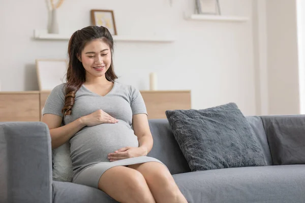 幸せな妊娠中のアジアの女性はソファに座って自宅で彼女の大きな腹を撫でて 将来の生活で楽しむ若い女性の妊娠は自宅でリラックス 母と妊娠の概念 ソフトフォーカス — ストック写真