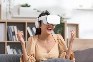 Asyalı kadın VR kulaklık takıyor ve giyilebilir sanal gerçeklik dijital yenilik teknolojisi ile mutlu anlar yaşıyor. Heyecanlı ve mutlu gülümseyen kız VR gözlüklerinden izliyor. Akıllı aygıt.
