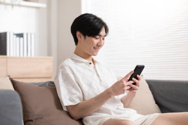 Asyalı adam iyi bir haber almış gibi cep telefonuyla gülümsüyor. Adam cep telefonu ekranından çok memnun görünüyor. Teknoloji bize kolaylık sağlıyor ve dünyayı küçültüyor..