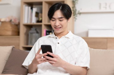 Asyalı adam iyi bir haber almış gibi cep telefonuyla gülümsüyor. Adam cep telefonu ekranından çok memnun görünüyor. Teknoloji bize kolaylık sağlıyor ve dünyayı küçültüyor..