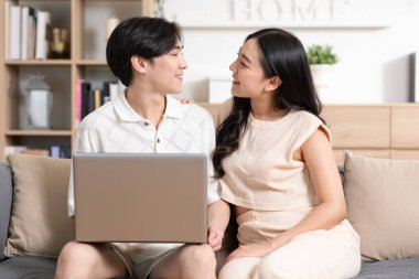 Asyalı genç bir çift kanepeye ya da kanepeye oturup dizüstü bilgisayarın gülüşüne bakıp birlikte gülüyorlar. Neşeli aşıklar internette sörf yapıyor ve sosyal medya tatillerini rahat bir evde geçiriyor. Sevgililer Günü