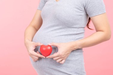 Hamile bir kadının göbeğine sarılıp, kalbini pembeye, mutluluğu pembeye çeviren, genç bir kadının hamileliğinin tadını çıkaran, aşkla, annelikle ve hamile kalmayla rahatlayan parmağını kapat.