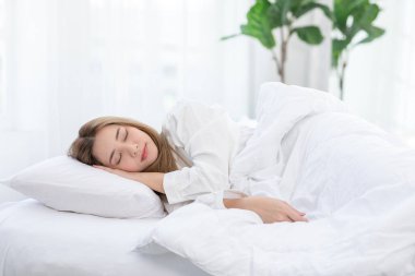 Güzel, Çekici, Asyalı bir kadın sabahları rahat bir yatak odasında uzanıp tatlı rüyalar görüyor. Rahatlayın ve rahatlayın. Sağlıklı, genç bir bayan, evde yatma vaktiyle uyuyor.